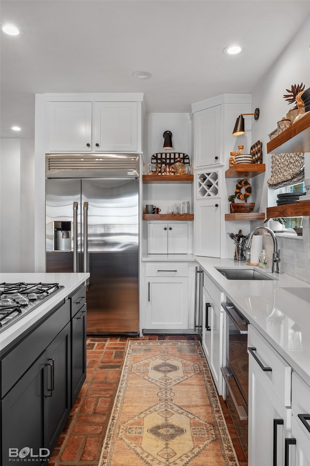 kitchen with appliances with stainless steel finishes, white cabinets, backsplash, light stone countertops, and sink