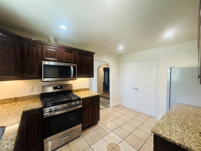 kitchen with light stone countertops, stainless steel appliances, light tile patterned floors, and dark brown cabinetry