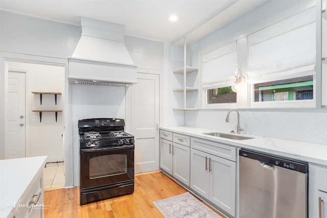 kitchen featuring black gas stove, dishwasher, sink, custom range hood, and light hardwood / wood-style flooring