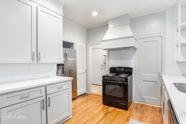 kitchen with white cabinets, custom exhaust hood, stainless steel appliances, light stone countertops, and light hardwood / wood-style floors