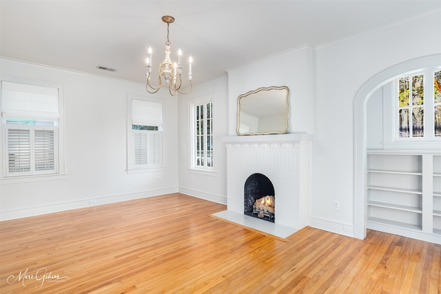 unfurnished living room featuring built in shelves, ornamental molding, wood-type flooring, an inviting chandelier, and a fireplace