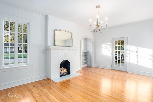 unfurnished living room featuring wood-type flooring, an inviting chandelier, a brick fireplace, and crown molding