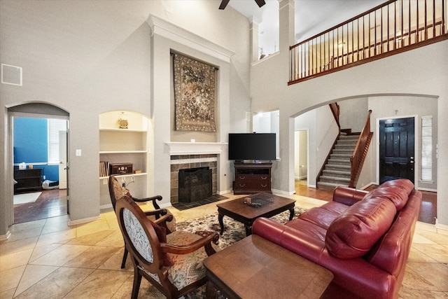 living room featuring light tile patterned floors, built in features, a high ceiling, and a tile fireplace