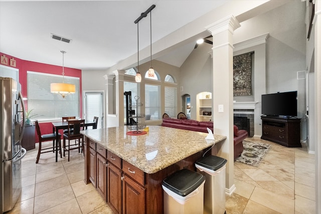 kitchen featuring light stone counters, hanging light fixtures, a kitchen island, and stainless steel refrigerator