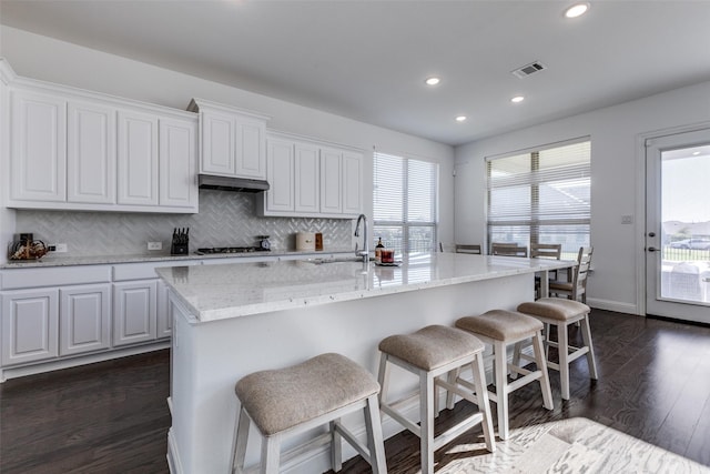 kitchen with sink, white cabinets, a kitchen breakfast bar, dark wood-type flooring, and a center island with sink