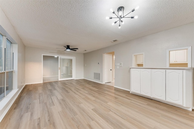 spare room featuring ceiling fan with notable chandelier, light wood-type flooring, and a textured ceiling