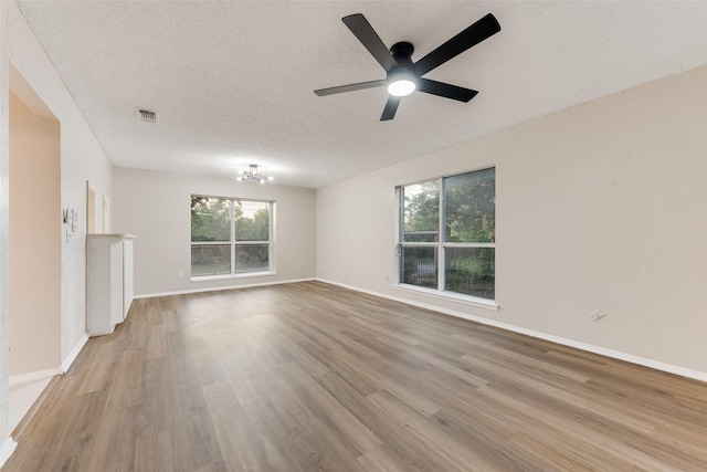 unfurnished living room with ceiling fan with notable chandelier, a textured ceiling, and light wood-type flooring