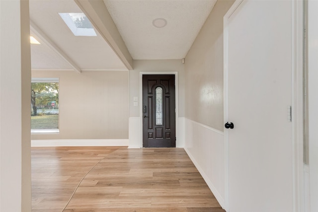 entrance foyer with vaulted ceiling with skylight, a textured ceiling, and light hardwood / wood-style flooring