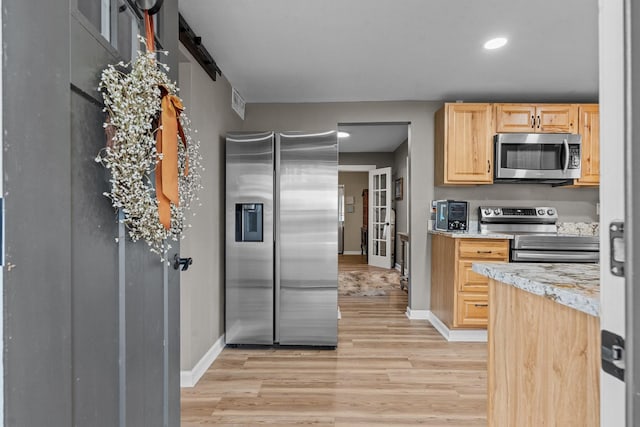 kitchen with stainless steel appliances, light stone countertops, light brown cabinetry, and light hardwood / wood-style floors