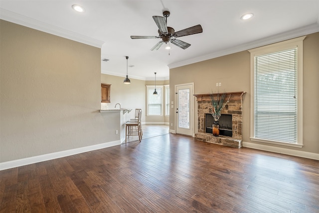 unfurnished living room with crown molding, a stone fireplace, ceiling fan, and dark wood-type flooring