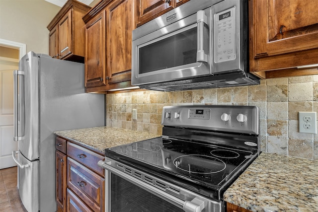 kitchen with light stone countertops, decorative backsplash, appliances with stainless steel finishes, and light tile patterned floors