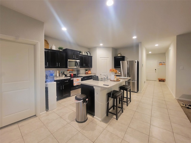 kitchen with light tile patterned flooring, stainless steel appliances, a kitchen bar, a kitchen island with sink, and sink