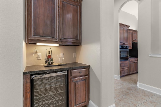 bar with light tile patterned floors, wine cooler, oven, and baseboards