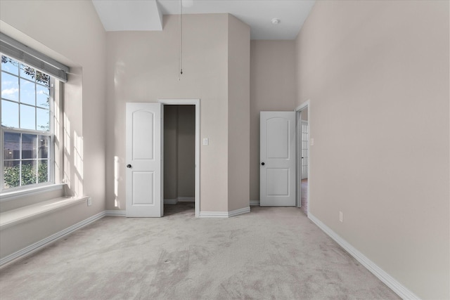 unfurnished bedroom featuring light colored carpet, a towering ceiling, baseboards, and multiple windows