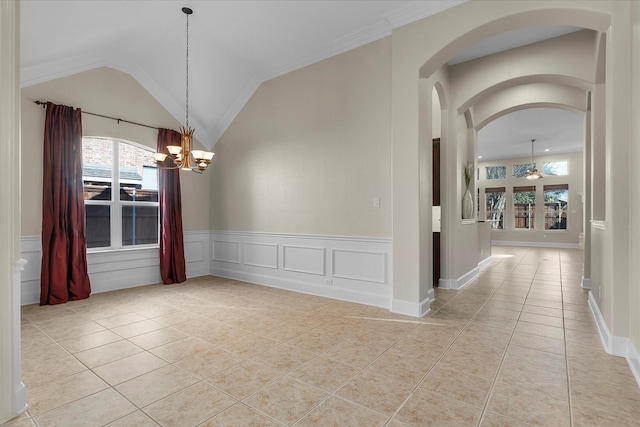 empty room featuring light tile patterned floors, a decorative wall, wainscoting, vaulted ceiling, and ceiling fan with notable chandelier