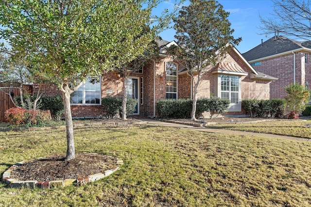 view of property hidden behind natural elements featuring a front lawn and brick siding