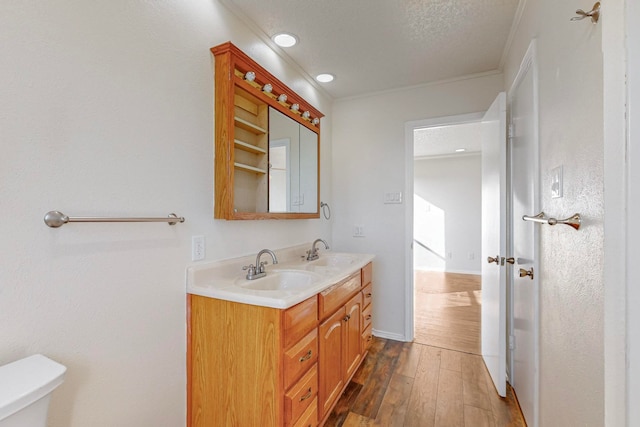 bathroom featuring a textured ceiling, hardwood / wood-style floors, crown molding, vanity, and toilet