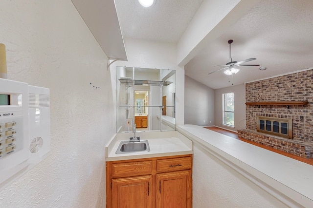 kitchen featuring a textured ceiling, sink, ceiling fan, and a brick fireplace