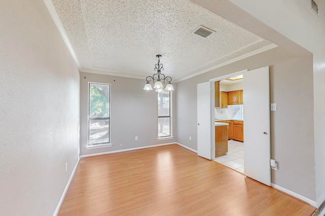 unfurnished dining area featuring a textured ceiling, ornamental molding, light hardwood / wood-style flooring, and a notable chandelier