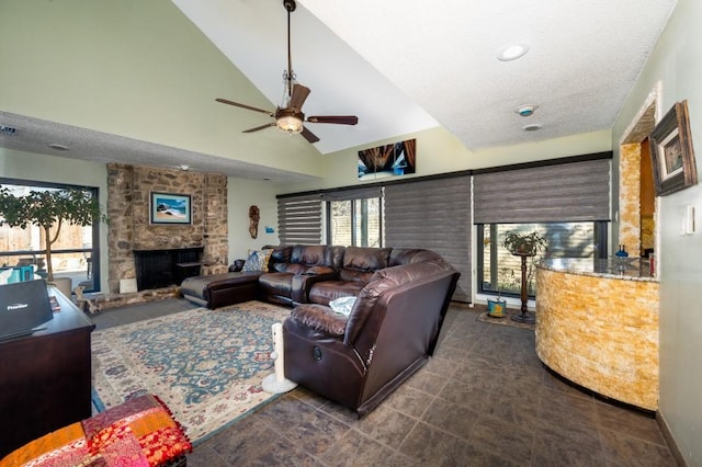 living room featuring ceiling fan, a stone fireplace, high vaulted ceiling, and a textured ceiling