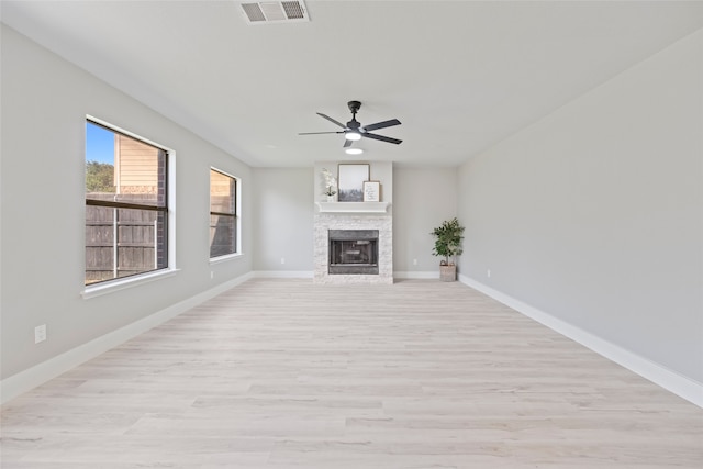 unfurnished living room featuring a stone fireplace, ceiling fan, and light hardwood / wood-style floors