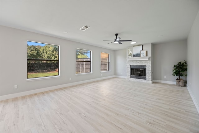 unfurnished living room featuring ceiling fan, a stone fireplace, and light wood-type flooring