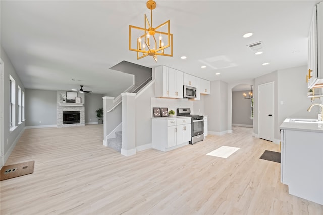 kitchen featuring white cabinets, appliances with stainless steel finishes, light hardwood / wood-style flooring, and a stone fireplace