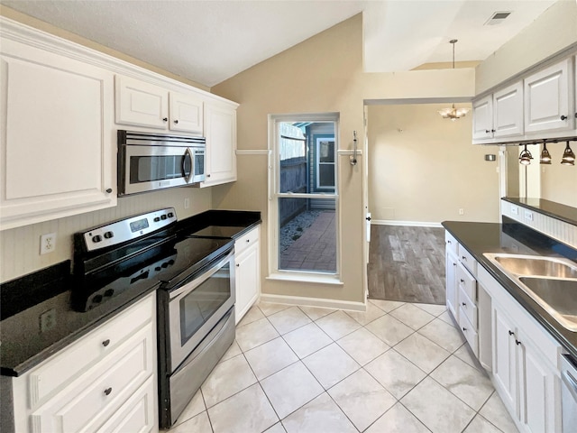 kitchen featuring white cabinets, lofted ceiling, light tile patterned floors, a chandelier, and appliances with stainless steel finishes