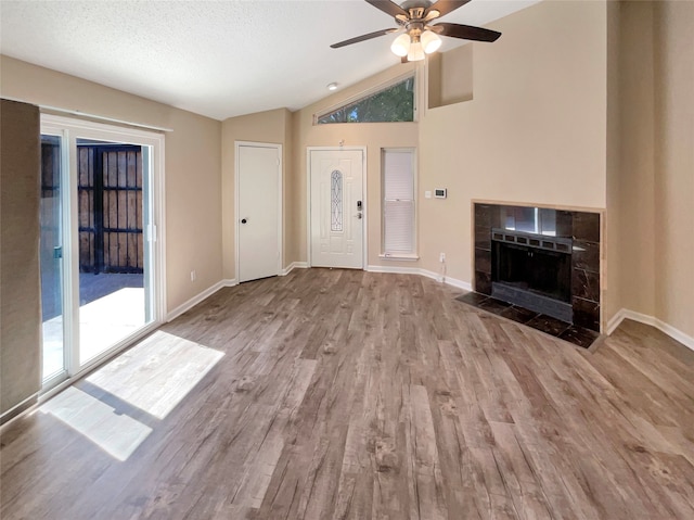 unfurnished living room featuring light wood-type flooring, vaulted ceiling, a textured ceiling, and a tile fireplace