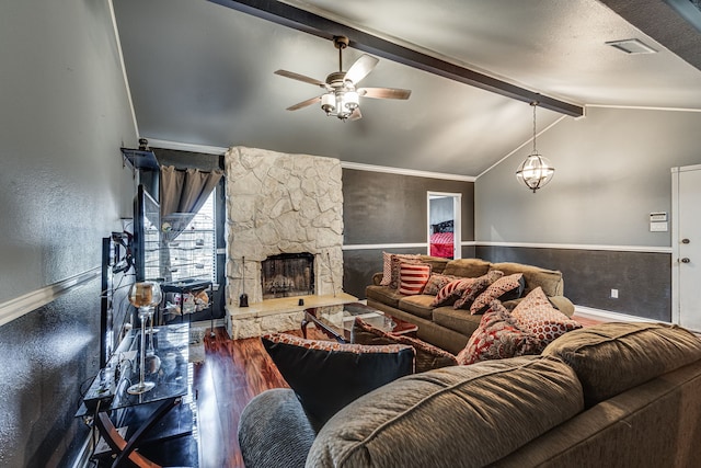 living room with vaulted ceiling with beams, hardwood / wood-style floors, a stone fireplace, ornamental molding, and ceiling fan