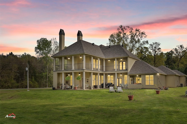 back house at dusk featuring a balcony and a yard