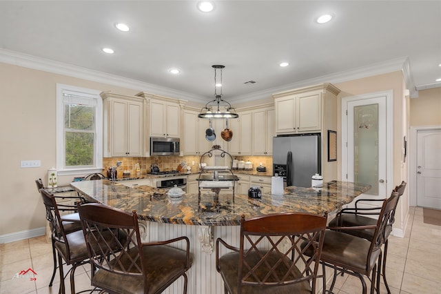 kitchen with a kitchen bar, appliances with stainless steel finishes, decorative light fixtures, dark stone countertops, and cream cabinets