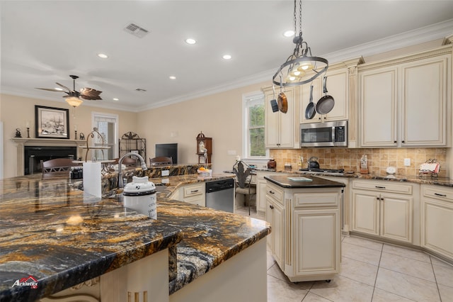 kitchen with a center island, cream cabinetry, appliances with stainless steel finishes, decorative light fixtures, and dark stone countertops