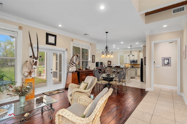 living room featuring light wood-type flooring, ornamental molding, french doors, and a notable chandelier