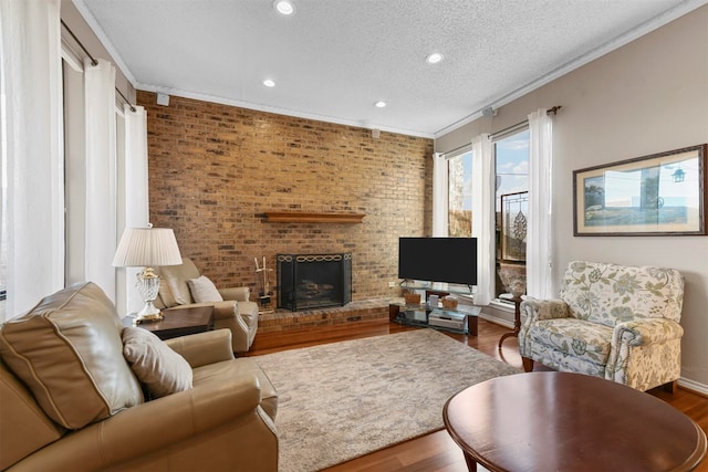 living room with hardwood / wood-style flooring, brick wall, crown molding, a brick fireplace, and a textured ceiling