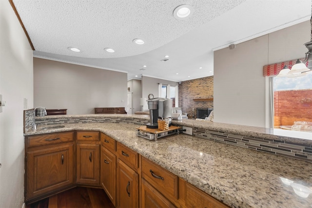 kitchen featuring a large fireplace, dark hardwood / wood-style flooring, a textured ceiling, ornamental molding, and light stone counters