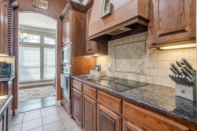 kitchen with appliances with stainless steel finishes, decorative backsplash, light tile patterned floors, crown molding, and dark stone counters