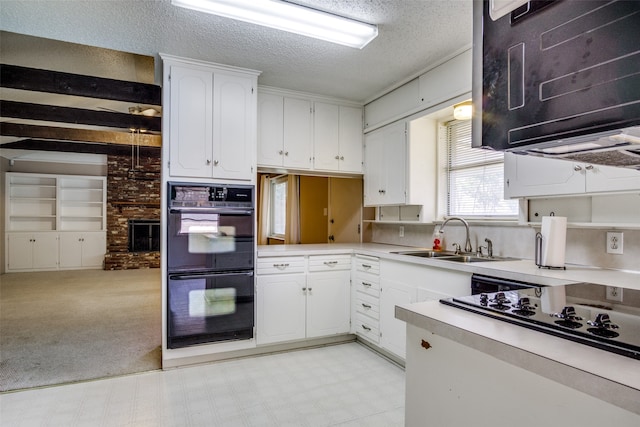 kitchen featuring double oven, sink, a brick fireplace, white cabinetry, and a textured ceiling