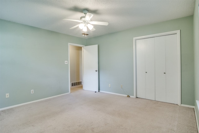 unfurnished bedroom with a closet, ceiling fan, light carpet, and a textured ceiling