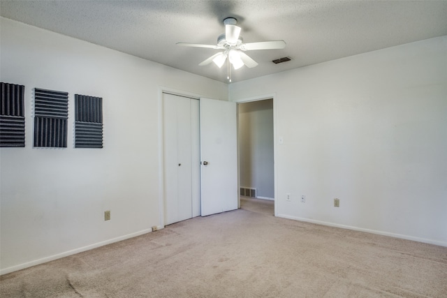 unfurnished bedroom with light carpet, a closet, a textured ceiling, and ceiling fan