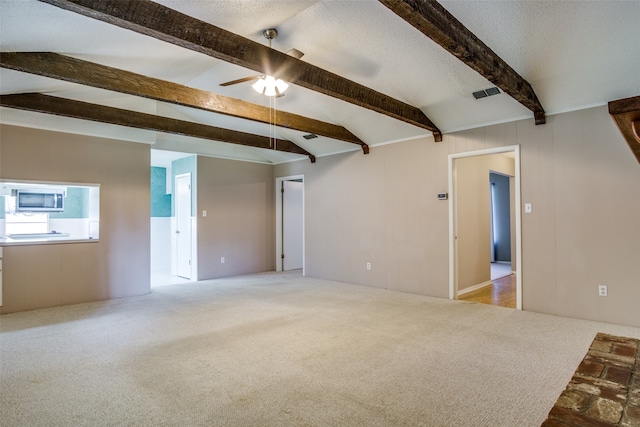 interior space featuring ceiling fan, lofted ceiling with beams, a textured ceiling, and light colored carpet