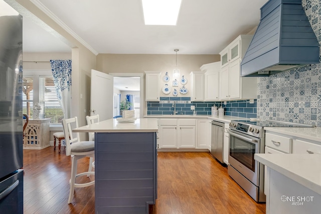 kitchen with pendant lighting, white cabinets, light hardwood / wood-style flooring, appliances with stainless steel finishes, and custom range hood