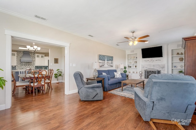 living room featuring wood-type flooring, ceiling fan with notable chandelier, built in features, and ornamental molding