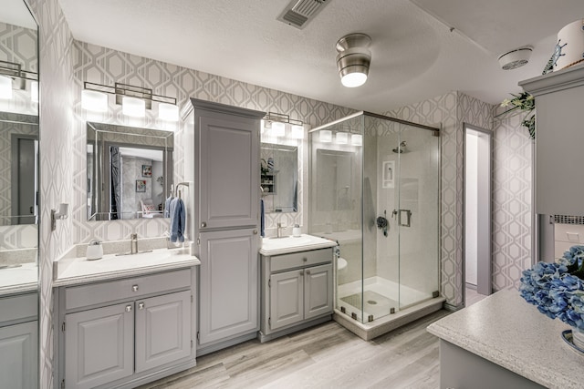 bathroom with wood-type flooring, a textured ceiling, a shower with shower door, ceiling fan, and vanity