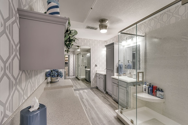 bathroom with ceiling fan, vanity, an enclosed shower, a textured ceiling, and hardwood / wood-style flooring