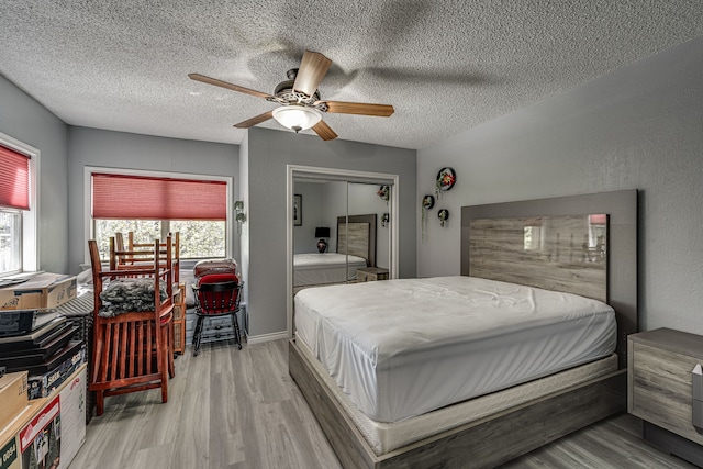 bedroom with ceiling fan, a textured ceiling, light hardwood / wood-style floors, and multiple windows