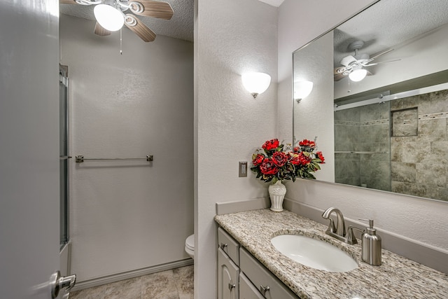 bathroom featuring a textured ceiling, a shower with shower door, ceiling fan, vanity, and toilet