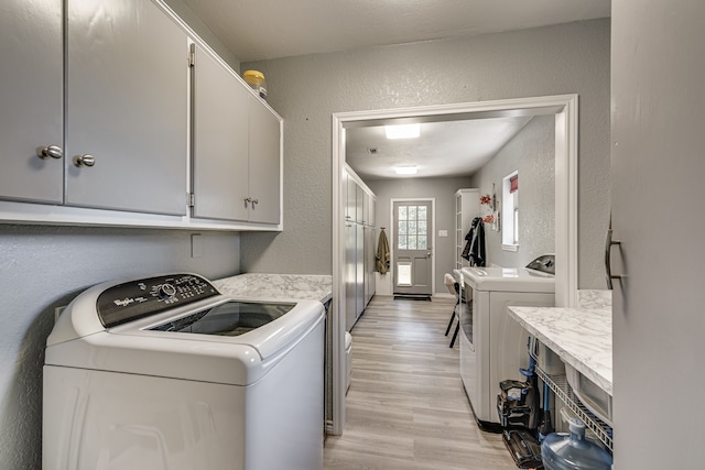 laundry room featuring washing machine and clothes dryer, light hardwood / wood-style floors, and cabinets