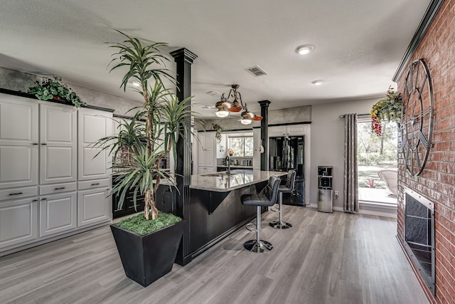 kitchen with light stone counters, a textured ceiling, an island with sink, light hardwood / wood-style flooring, and ceiling fan