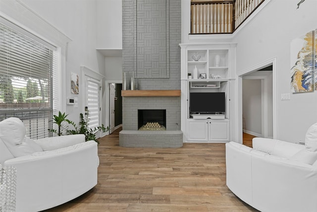 living room with light hardwood / wood-style floors, a fireplace, and a high ceiling